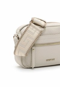 Crossbody taske i blødt beige læder med en tekstureret overflade, prydet med en dekorativ rem i creme med geometriske mønstre og guldfarvede hardware detaljer.
