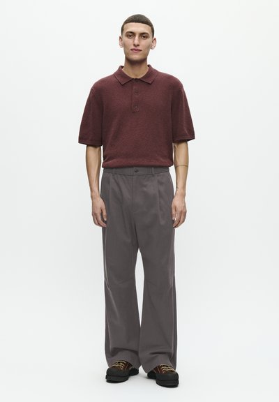 Cămașă polo texturată de culoare vișinie, cu mâneci scurte și trei butoane, asortată cu pantaloni largi gri și pantofi cu platformă negri.