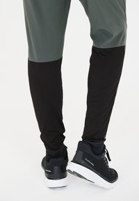 Idrottsbyxor med en grå övre sektion och en svart nedre sektion, tillverkade av stretchigt material. Kombineras med svarta sneakers med vita sulor.