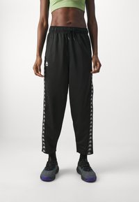 Pantaloni sportivi neri con vita elastica e cordoncino. Presentano strisce bianche sui lati con un motivo di logo ripetuto. Tessuto morbido e leggero.