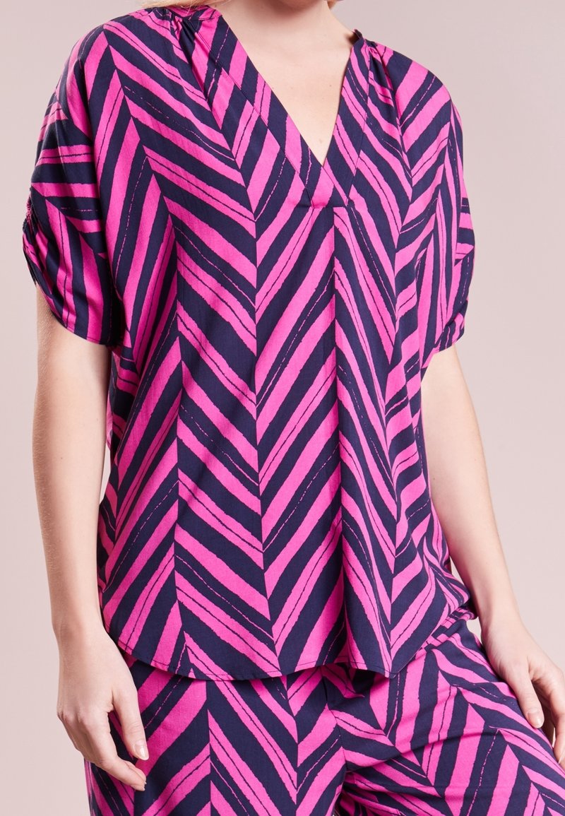 Blusa a righe chevron rosa e blu navy con maniche corte, scollatura a V e vestibilità comoda. Tessuto leggero con una texture morbida.