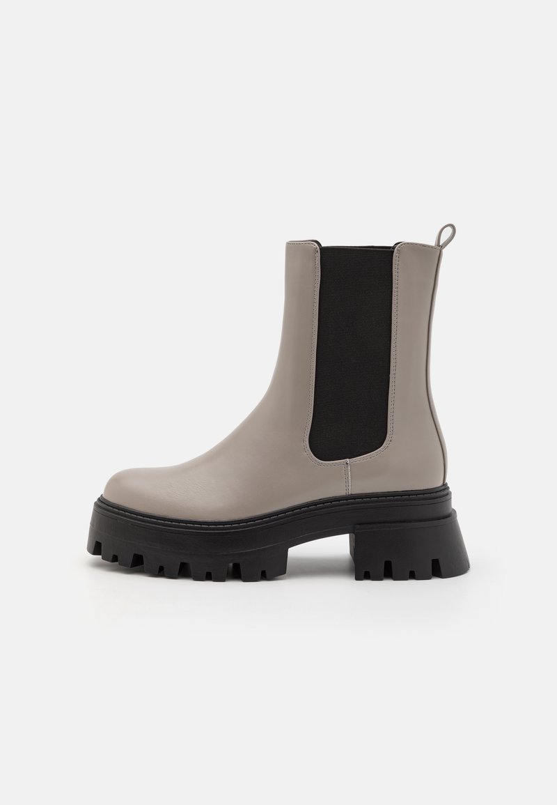 Bottine Chelsea en cuir taupe avec semelle crantée épaisse noire, panneaux latéraux élastiques et languette à l'arrière, montrée de profil.