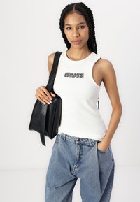 Hvid ribbet tanktop med "MUSE" trykt i sort og sølv accenter, parret med lyseblå loose-fit denimjeans og en sort læder håndtaske.