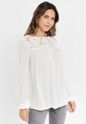 White long-sleeve blouse with lace detailing at the neckline, textured fabric, flowing silhouette, and a relaxed fit.