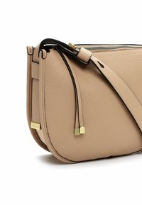 Beige Leder Umhängetasche mit einer strukturierten Oberfläche, schwarzen Akzenten, goldenen Beschlägen und einem Reißverschluss. Mit dekorativen Quasten und einem Markenetikett.