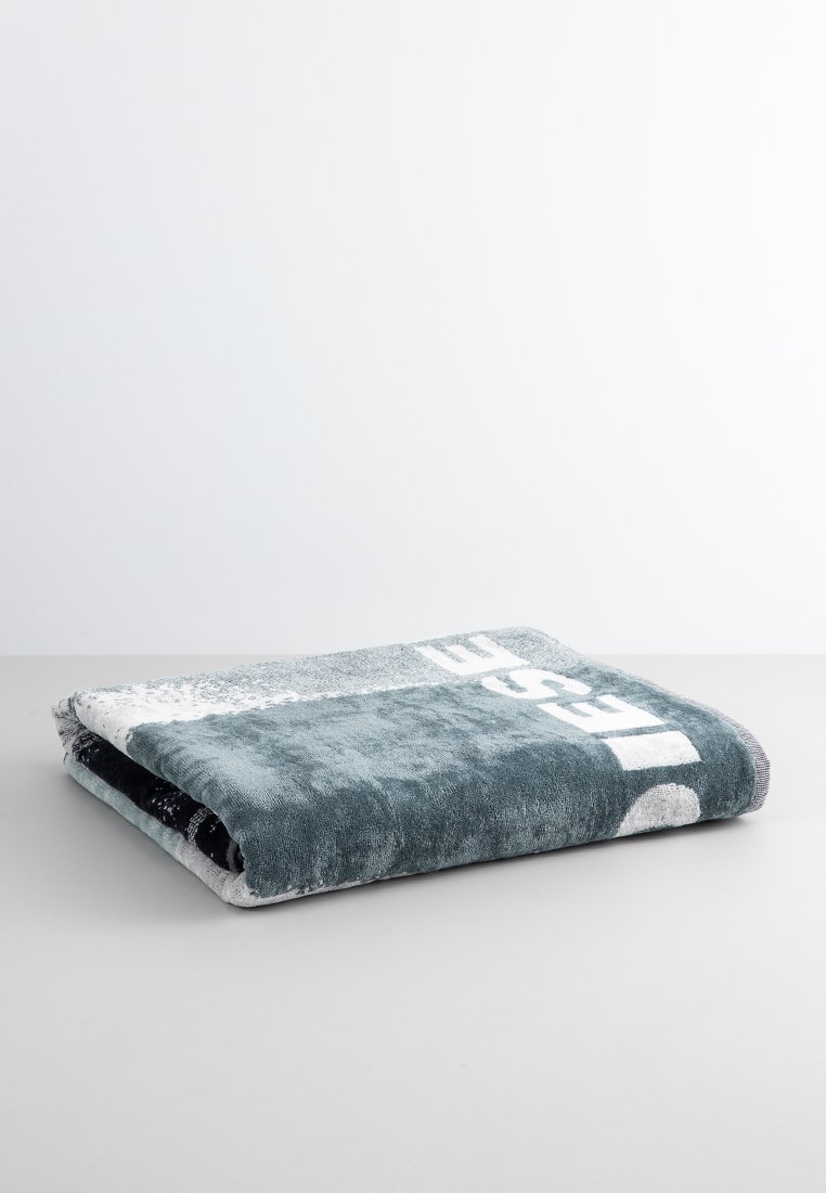 Plaid en peluche gris-bleu avec un grand design de logo blanc, plié soigneusement, avec une texture lisse et un motif de dégradé subtil.