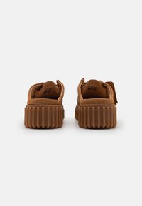Brown suede sneakers with a thick, ribbed rubber sole and wide opening. Features minimal stitching and a small pull tab at the back.
