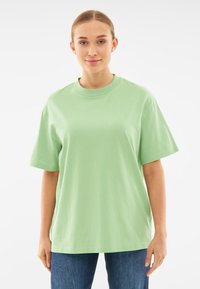 Jasnozielona bawełniana koszulka z okrągłym dekoltem, krótkimi rękawami i luźnym krojem, w połączeniu z niebieskimi dżinsami. Bez wzorów ani akcentów.