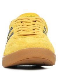 Gele suède sneaker met zwarte strepen, ronde neus, platte gumzool en bijpassend geel logo op de tong; gestructureerde bovenkant voor grip.