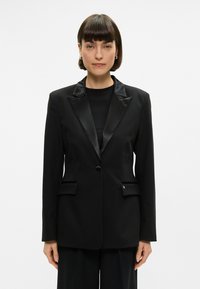 Černý blazer se saténovými klopami, uzávěr na jeden knoflík, dvě přední kapsy a upravený střih. Hladká textura, strukturovaný design.