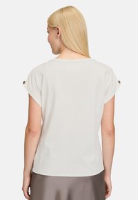 Witte top met korte mouwen en kapmouwen, voorzien van decoratieve knopen op de schouder, gemaakt van een zachte stof en met een ontspannen pasvorm.