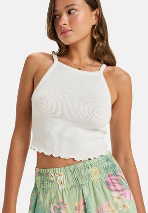 White ribbed crop top with scalloped hem, paired with light green floral printed high-waisted pants featuring an elastic waistband.