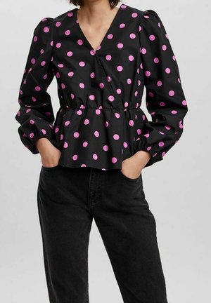 Schwarze Bluse mit pinken Punkten, tiefem V-Ausschnitt, elastischem Bund und Puffärmeln. Präsentiert mit schwarzen Jeans für den Kontrast.