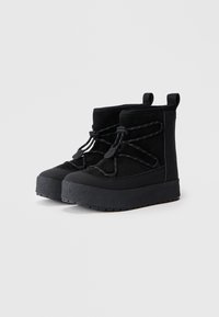 Zwarte enkelboots van suède en rubber, met een dikke, gestructureerde zool en elastische veters met reflecterende accenten.