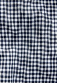 Tela de cuadros en tonos marino y blanco, con un patrón a cuadros de tamaño uniforme, confeccionada en un textil suave con un sutil brillo.