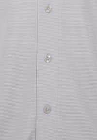 Tissu blanc texturé avec trois boutons ronds transparents cousus en ligne verticale sur le devant d'une chemise.