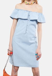 Vaalinen sininen farkkukangas olkapäältä paljastava mekko, jossa on rypytetty pääntie, etupainike ja istuva siluetti. Mukana värikkäitä renkaita ja ketjuhihnalla varustettu laukku.