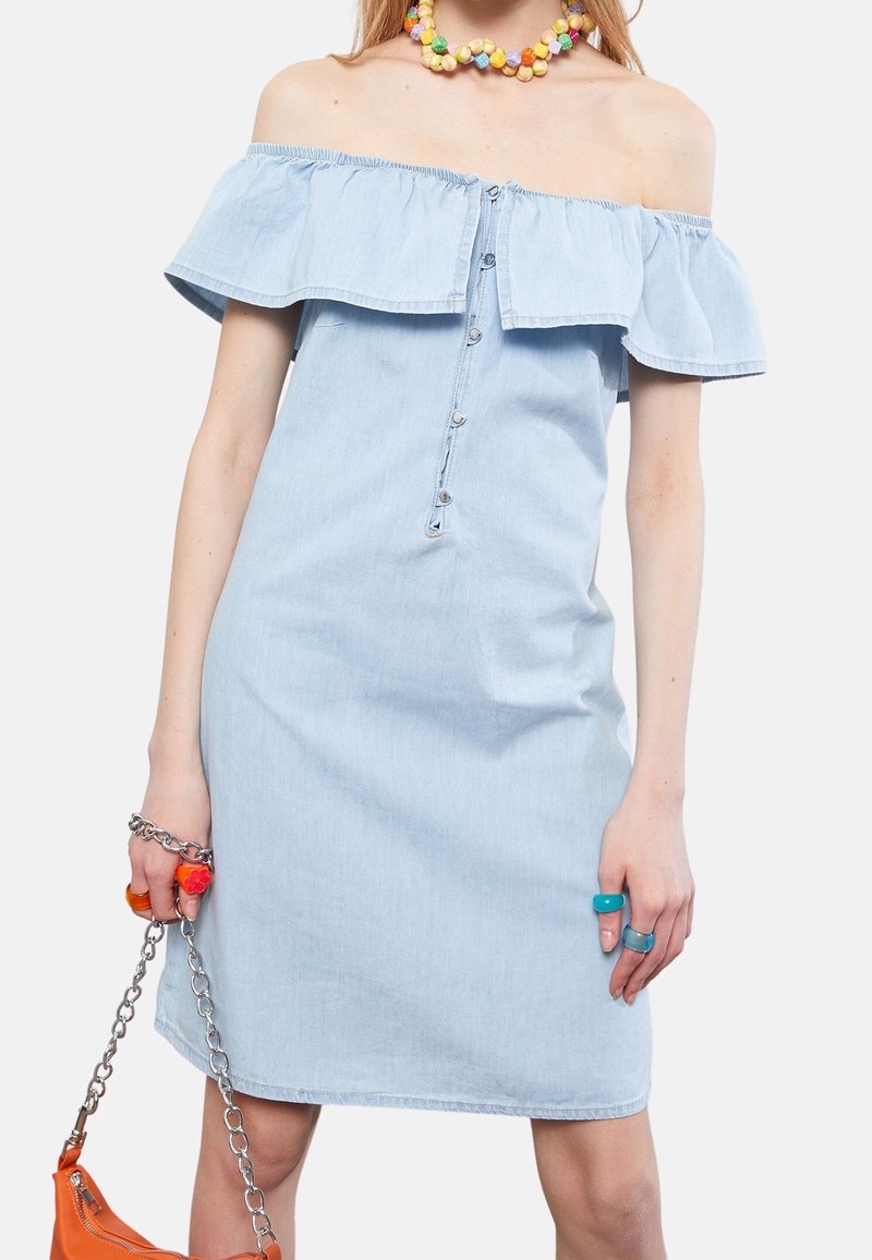 Vaalinen sininen farkkukangas olkapäältä paljastava mekko, jossa on rypytetty pääntie, etupainike ja istuva siluetti. Mukana värikkäitä renkaita ja ketjuhihnalla varustettu laukku.