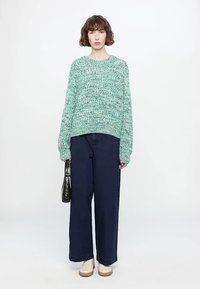 Fluffy, mint green knitted sweater with loose fit and round neckline, paired with wide-leg dark denim jeans and cream sneakers. Holding a black handbag.