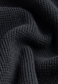 Tissu noir texturé avec un motif en nid d'abeille, créant une apparence douce et légèrement duveteuse. Le matériau semble chaud et accueillant.