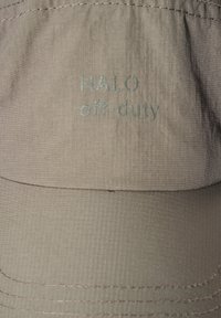 Beige keps i texturerad tyg med broderat "HALO" och "off-duty" i ljusblått. Strukturerad form med en bred skärm och stygn detaljer.