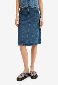 Denim midi kjol med vertikala sömmar, hög midja och avslappnad passform. Kombinerad med blå remsandaler och en kortblus i blått.