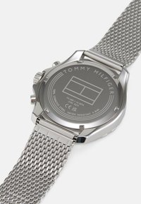 Edelstahl-Uhr mit einem Mesh-Armband, ausgestattet mit einem grauen Zifferblatt und graviertem Markennamen auf der Rückseite. Wasserdicht bis 5 bar.