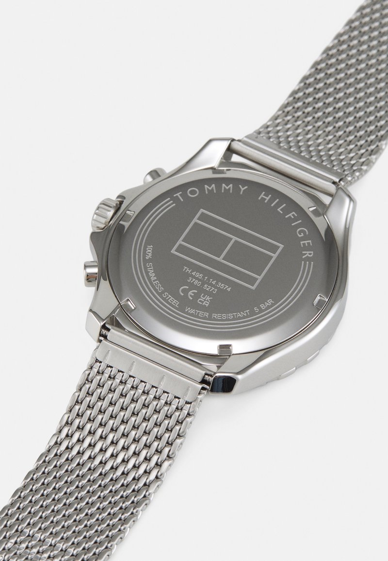 Reloj de acero inoxidable con correa de malla, que presenta una esfera gris y el nombre de la marca grabado en la parte posterior. Resistente al agua hasta 5 bares.