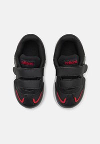Zapatillas deportivas negras con acentos rojos, parte superior de cuero texturizado, dos correas ajustables de Velcro y plantilla acolchada. Suela de goma blanca plana.