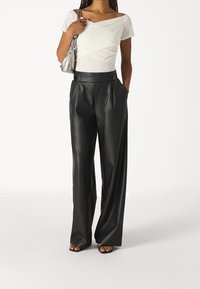 Svarta imitationläderbyxor med vida ben och hög midja samt två framfickor. Kombinerat med en åtsittande vit topp i ett mjukt material.