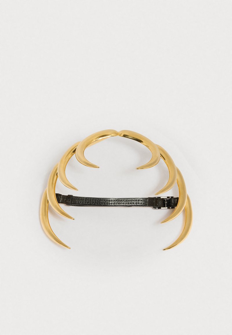 Zlatý drápovitý hlavový doplněk s matně černým nastavitelným páskem; obsahuje čtyři lesklé, zakřivené prvky nahoře pro dramatický vzhled.