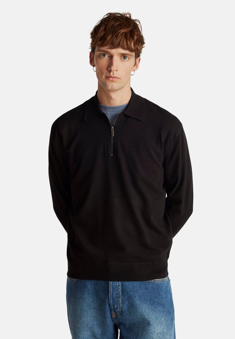 Pullover zip-up nero realizzato in tessuto morbido, con colletto e maniche lunghe, abbinato a jeans azzurri strappati.