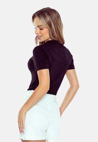 Czarna bluzka krótki rękaw z dopasowanym krojem, okrągłym dekoltem i gładką teksturą, w zestawie z jasnymi szortami o wysokim stanie.