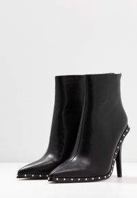 Mustat nahka ankle-bootit, joissa on terävä kärki, korkea stiletto-korko ja hopeiset niittiakselit pohjan ympäri. Vetoketjukiinnitys takana.