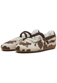 Bailarinas Puma en blanco con estampado de vaca marrón, que cuentan con dos correas elásticas marrones, material texturizado suave y suela de goma flexible.