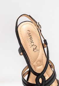 Sandalia negra de tiras con una plantilla beige suave. Presenta un estampado de logo, hebilla ajustable y suela texturizada para un mejor agarre.