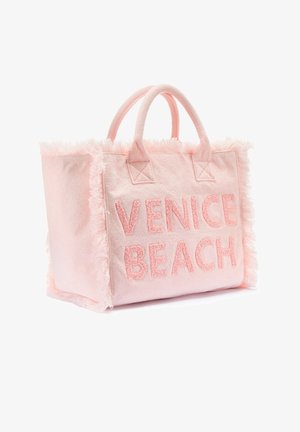 Pink fabric tote bag with plush fringe trim and embroidered "VENICE BEACH" text. Features dual fabric carry handles.