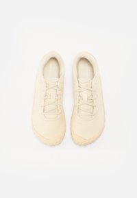 Light beige athletic shoes with a smooth synthetic upper, flat laces, and a textured rubber sole. Features a slightly elevated toe area.