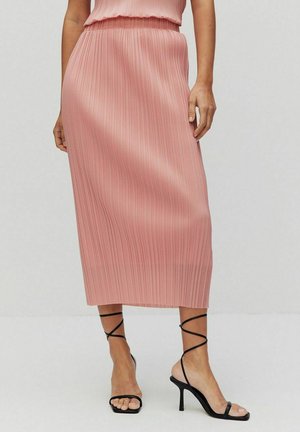 Jupe midi plissée rose en tissu léger avec une taille ajustée, associée à des sandales à talons squelettiques noires.