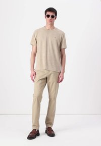 Beige t-paita lyhyillä hihoilla, vaaleanbeige housut ja ruskeat loafers-kengät. Mallilla on myös pyöreät mustat aurinkolasit. Yksinkertainen, rento asu.