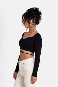 Black ribbed long-sleeve crop top with a V-neck and twisted strap design, paired with high-waisted cream pants.