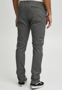 Grå bomullschinos med slim fit, med baklommer med knappelukking, og brukt med svarte sneakers. Glatt tekstur og strømlinjeformet design.