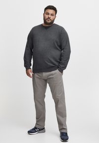 Pulover gri închis cu gât rotund, asortat cu pantaloni gri deschis și adidași sport bleumarin. Textură netedă, croială lejeră.
