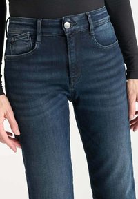 Jean taille haute bleu foncé en denim. Comprend une fermeture à bouton à l'avant, cinq poches et un léger délavage sur les jambes.