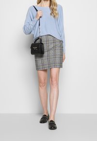 Ljusblå tröja med långa ärmar, grå rutig pennkjol, svart handväska med kedjerem och svarta loafers.