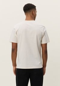T-shirt à manches courtes et col rond en coton beige clair, avec une coupe droite et sans logos ni motifs visibles.