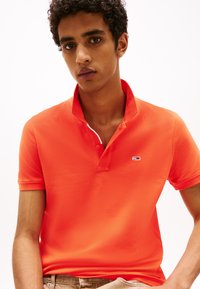 Oransje polo skjorte med klassisk krage, korte ermer og en liten logo aksent. Materialet ser glatt ut med en tettsittende design.