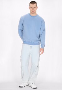 Felpa in cotone azzurro chiaro con maniche lunghe, scollatura tonda e polsini a costine abbinata a pantaloni cargo in denim chiaro con tasche laterali.