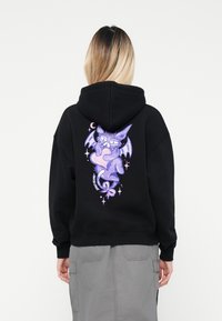 Zwarte hoodie met een paarse cartoonvleermuis met een bril en steraccenten op de achterkant. Zachte stof, standaard pasvorm en verstelbare capuchon.