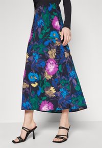 Falda larga floral en azul marino con flores multicolores, que cuenta con una cinturilla ancha y una silueta fluida. Combinada con sandalias negras de tacón.